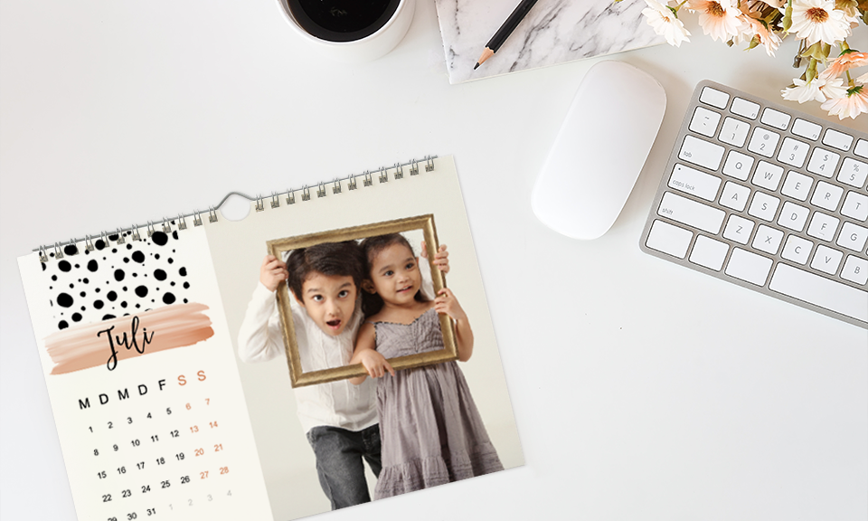 Monatskalender als Wandkalender auf Schreibtisch, daneben Tastatur und Kaffeetasse
