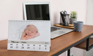 Ein Tischkalender mit Fotos, der auf einem Schreibtisch vor einem Laptop steht