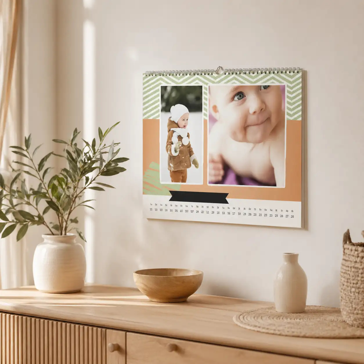 Monatskalender mit Babyfotos in einer hellen, wohnlichen Einrichtung über einem Holzsideboard
