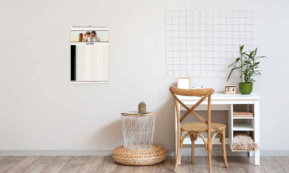 Ein Arbeitsplatz. Es hängt ein ein Wandkalender an der Wand. Der Familienplaner hat 5 Spalten und ein Familienfoto obendrüber