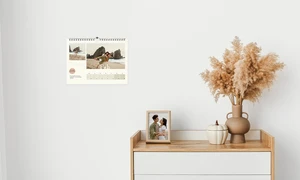 Ein Wandkalender hängt neben einem Schreibtisch, auf dem Fotos stehen