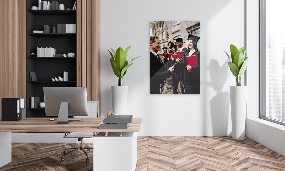 Schreibtisch mit Pflanze, im Hintergrund Alu dibond Direktdruck Wandbild mit College Absolventen